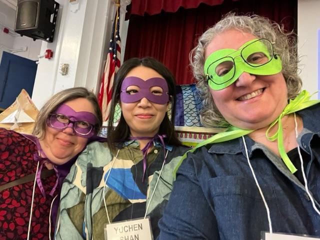 Three women smiling with superhero masks.