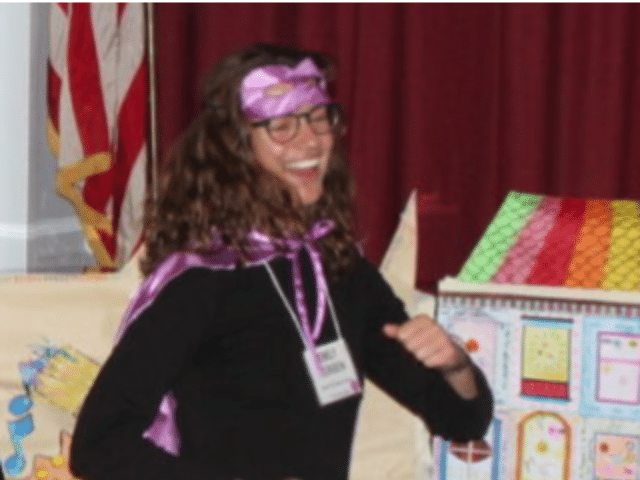 An African American woman with a purple super hero cape and eye mask.